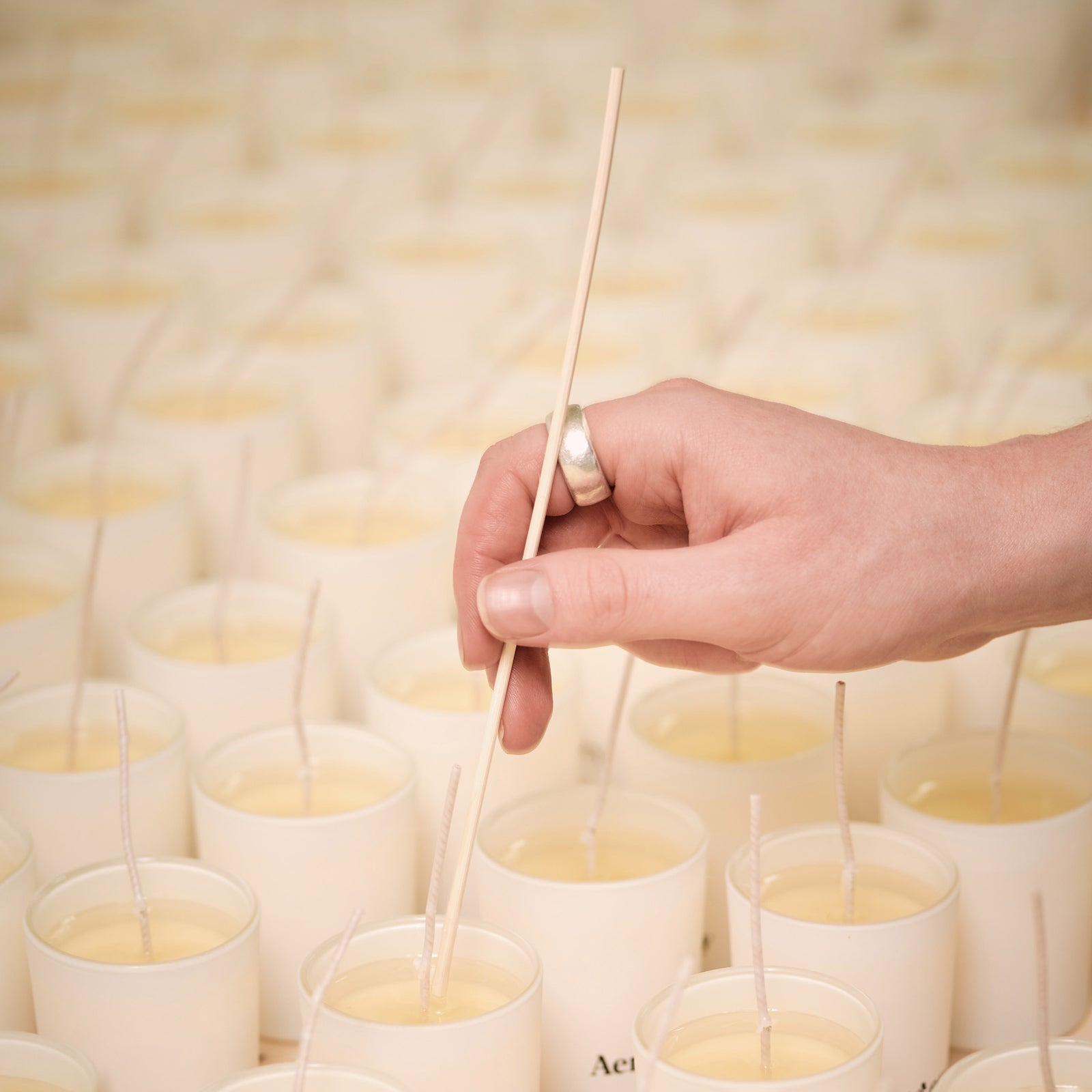hand using stick to remove any air bubbles in freshly poured candles