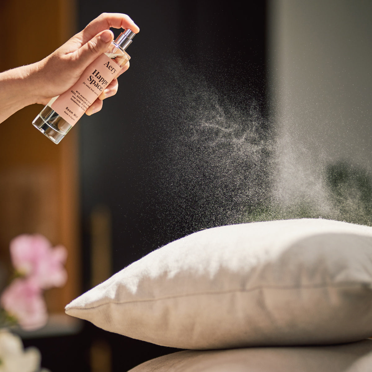 person spraying happy space room mist onto cushions