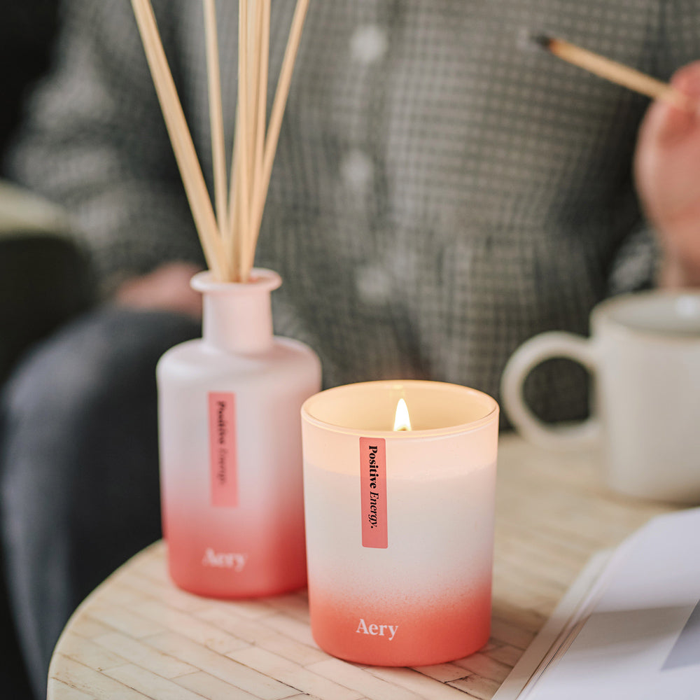 positive energy candle and matching diffuser on coffee table with person in the background