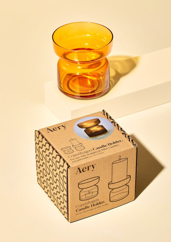 aery living orange coloured glass candle holder displayed next to product packaging on a cream coloured background