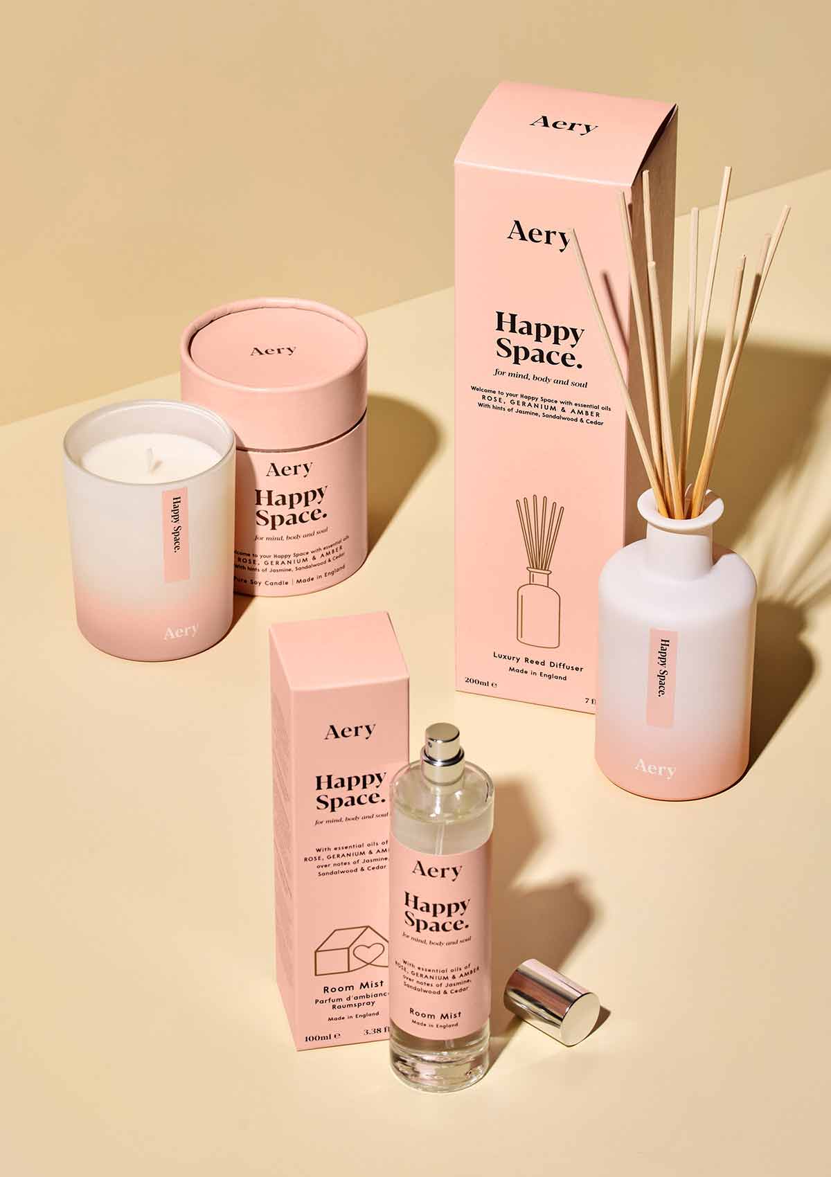 a selection of aery living happy space aromatherapy products. A room spray, reed diffuser and scented candle all displayed next to their product packaging