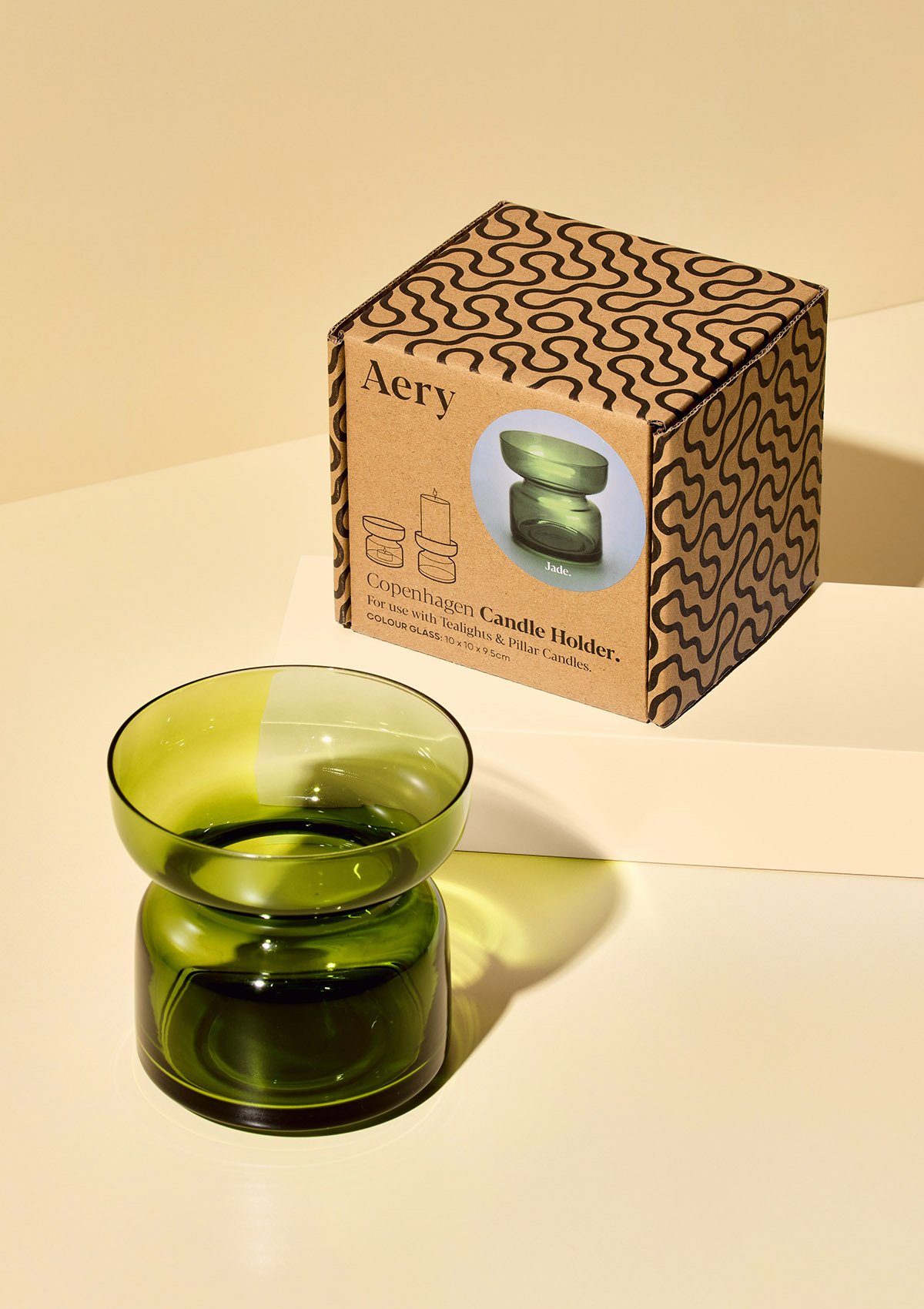 aery living dark green glass tea light holder displayed next to product background against a cream coloured background