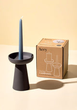 aery living tall charcoal ceramic candle holder with teal blue tapered candle displayed next to kraft product packaging against a yellow background