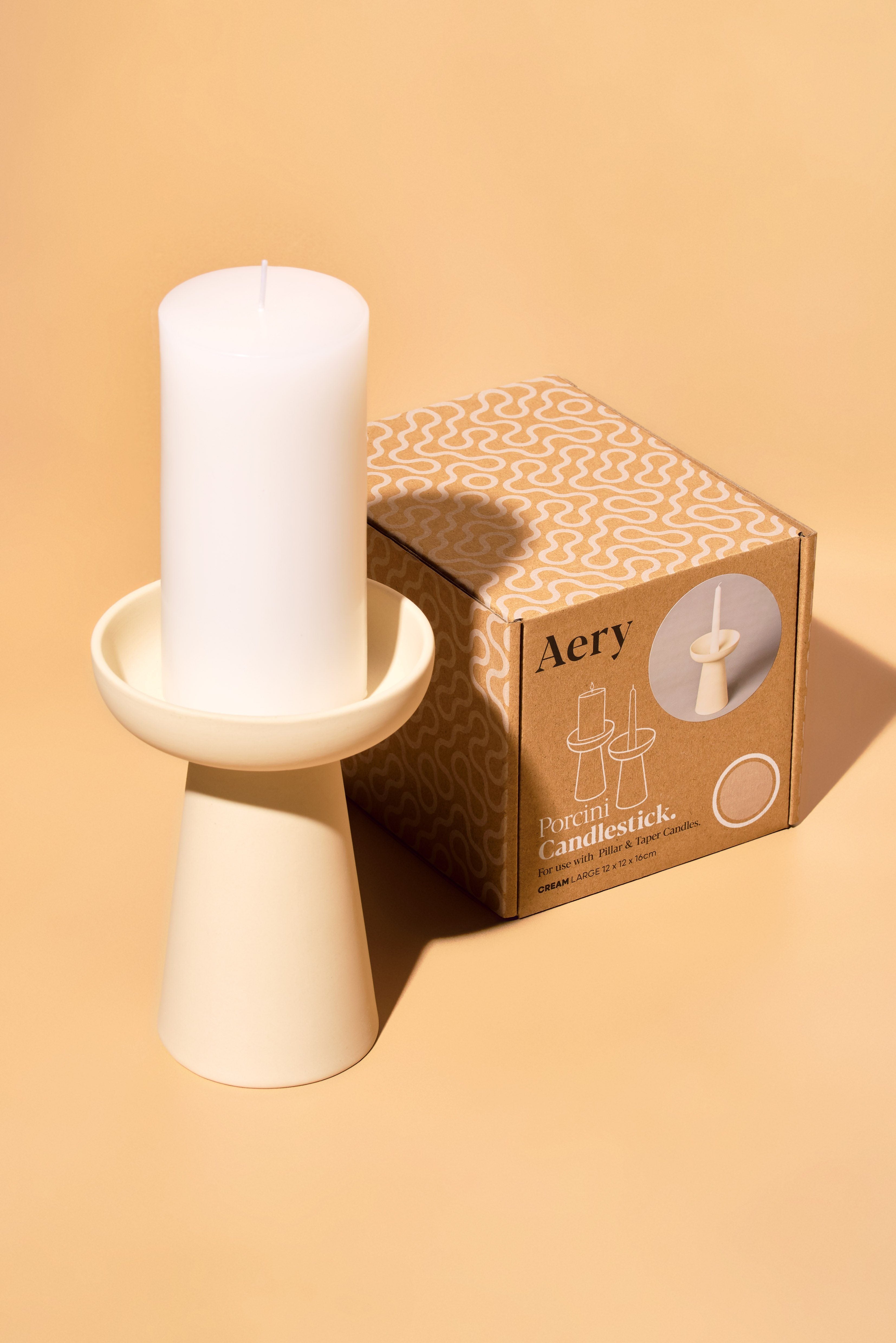 aery living tall cream ceramic candle holder displayed with white pillar candle and product packaging against an orange background