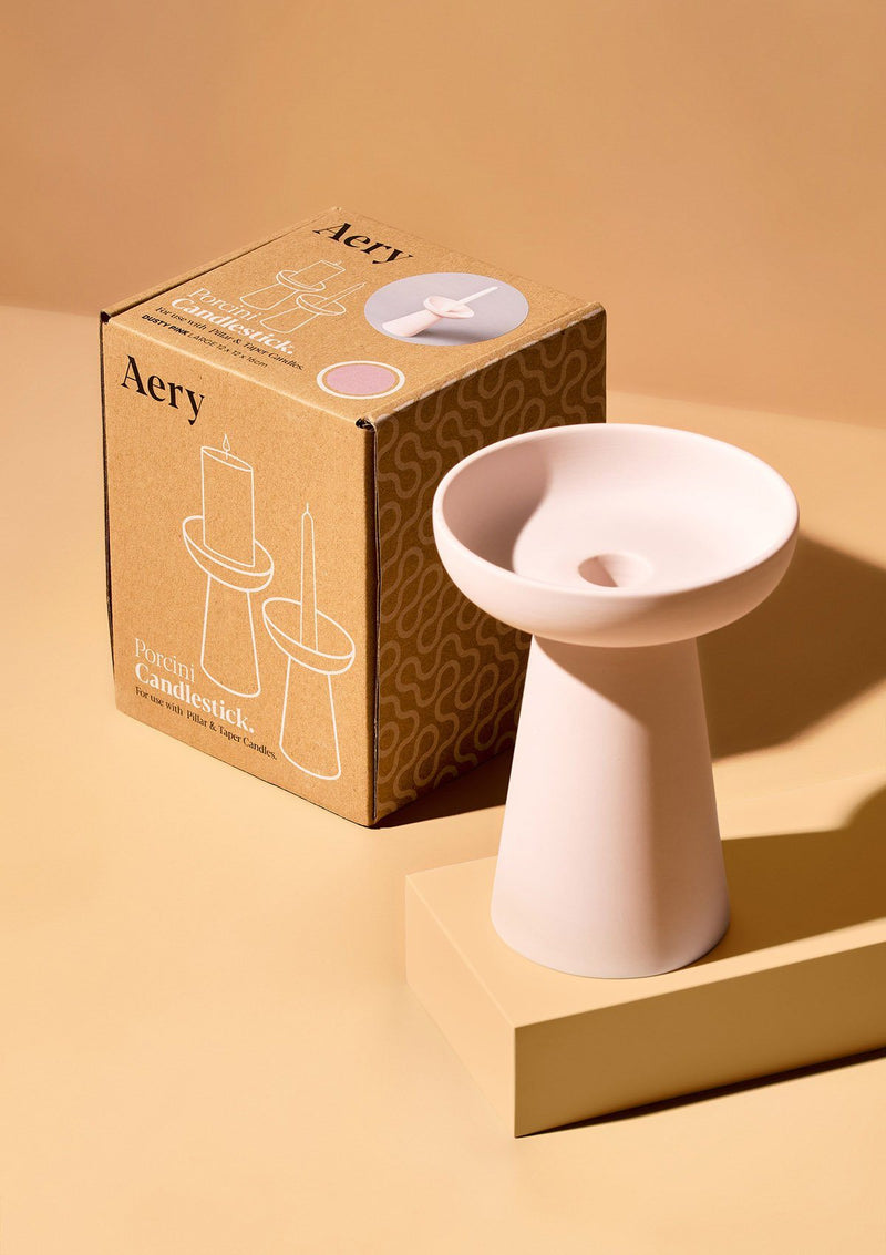 aery living tall ceramic candle holder in soft pink displayed next to product packaging against an orange background
