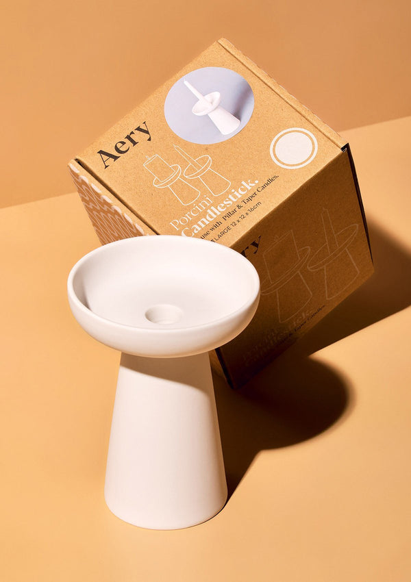 aery living matte white clay tall candle holder displayed next to product packaging against an orange background