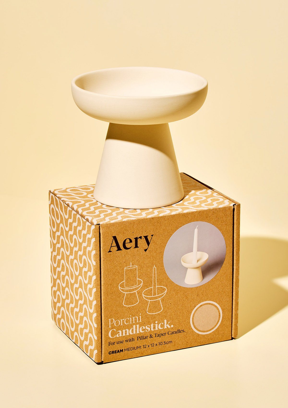 aery living cream ceramic candle holder displayed on top of product packaging against a yellow bacground