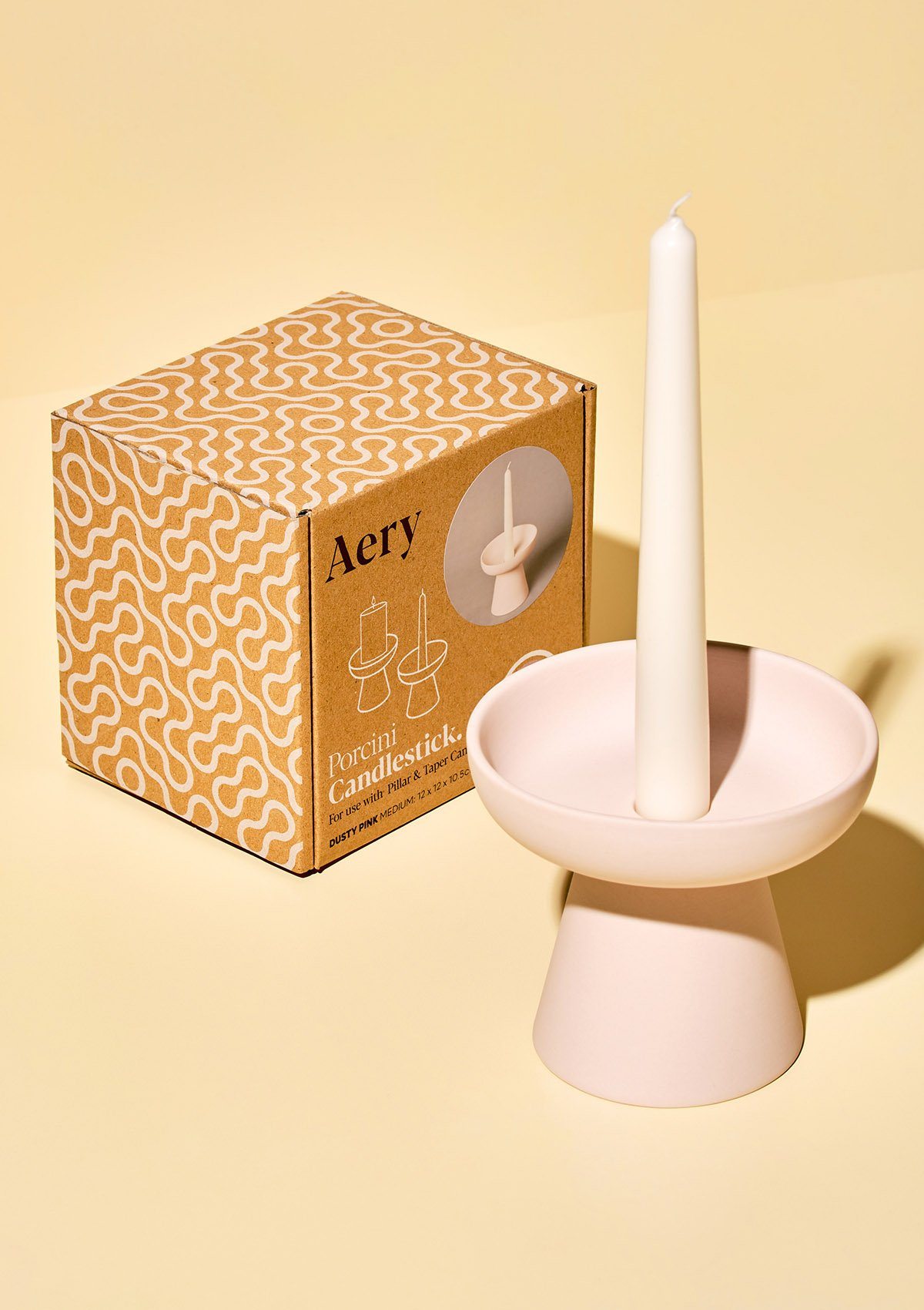 aery living soft pink ceramic candle holder displayed with white tapered candle and product packaging against a yellow background