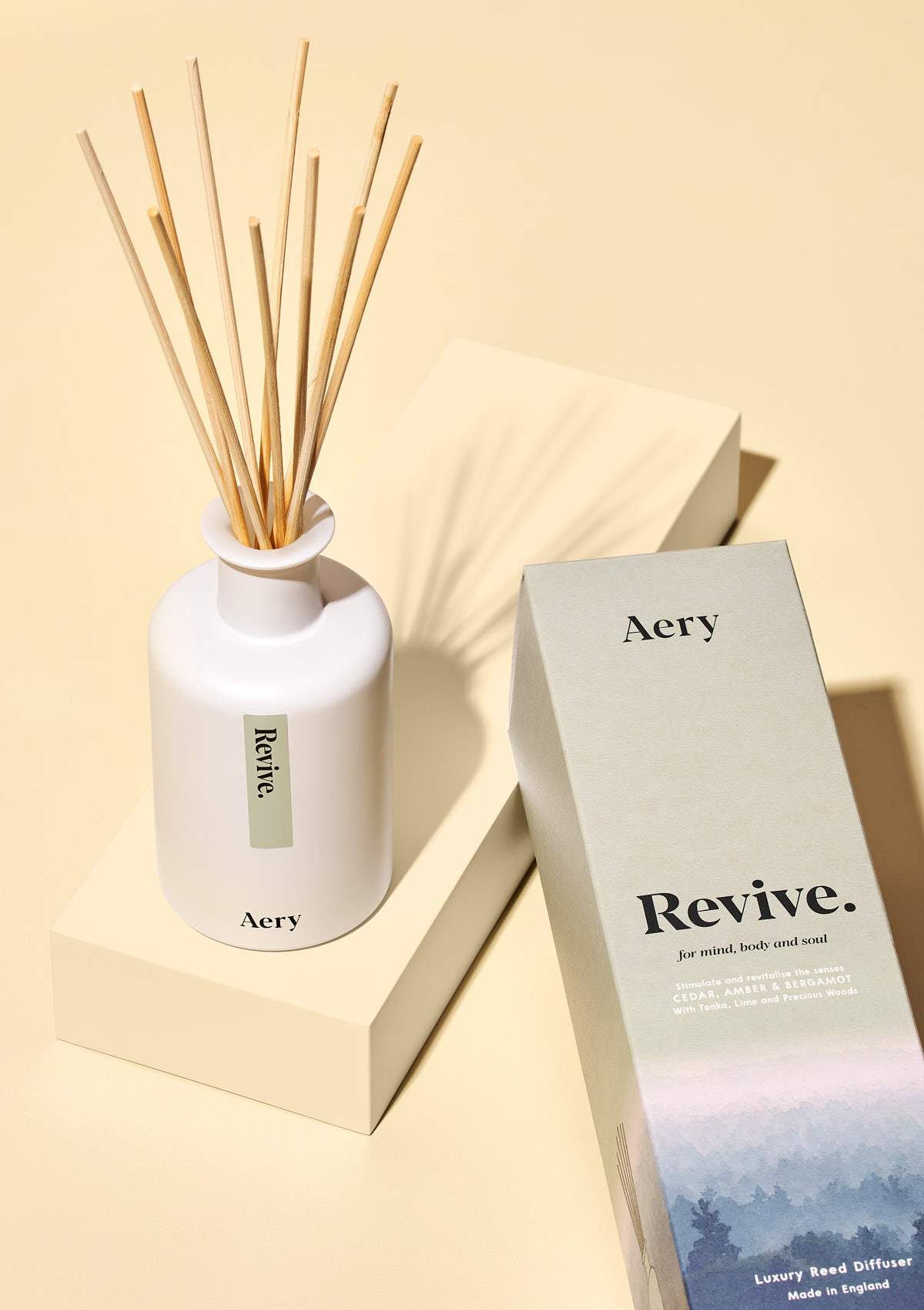 aery living revive reed diffuser next to green product packaging on a yellow background