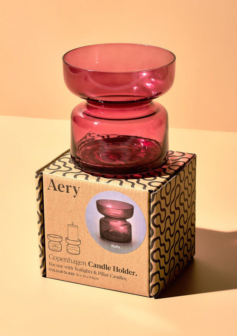 aery living pink coloured glass tea light holder displayed on top of decorative product packaging against an orange coloured background
