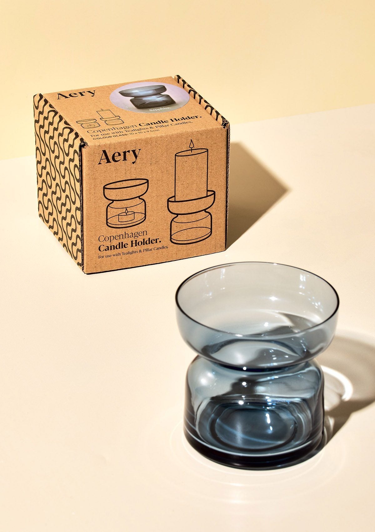aery living blue glass coloured tea light holder displayed next to product packaging on a cream coloured background